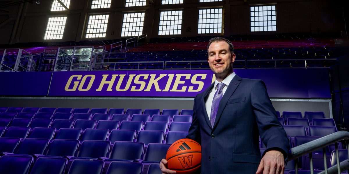 Danny Sprinkle stands holding a basketball in the stands of Hec Ed